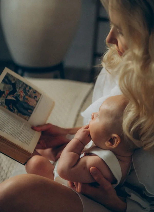 A mother reading a book while holding her baby.