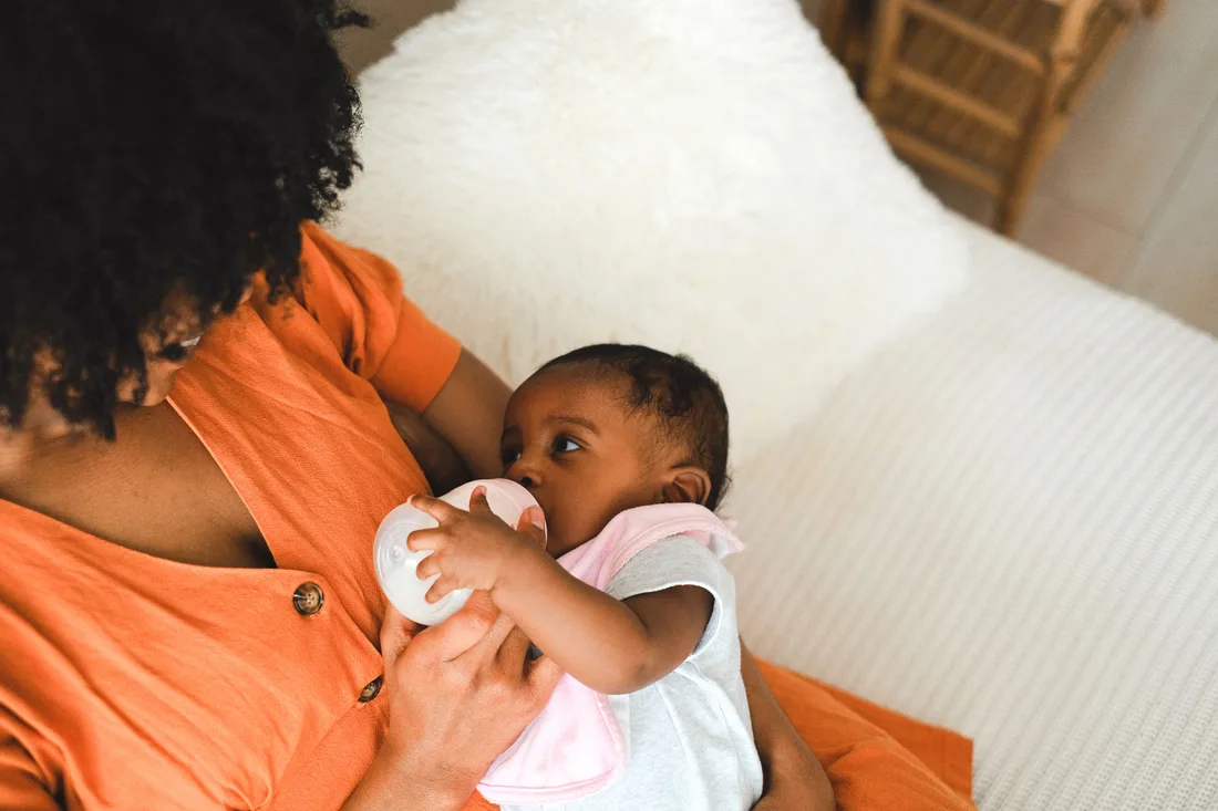 Caregiver supports an awake baby while holding a bottle during a feed.