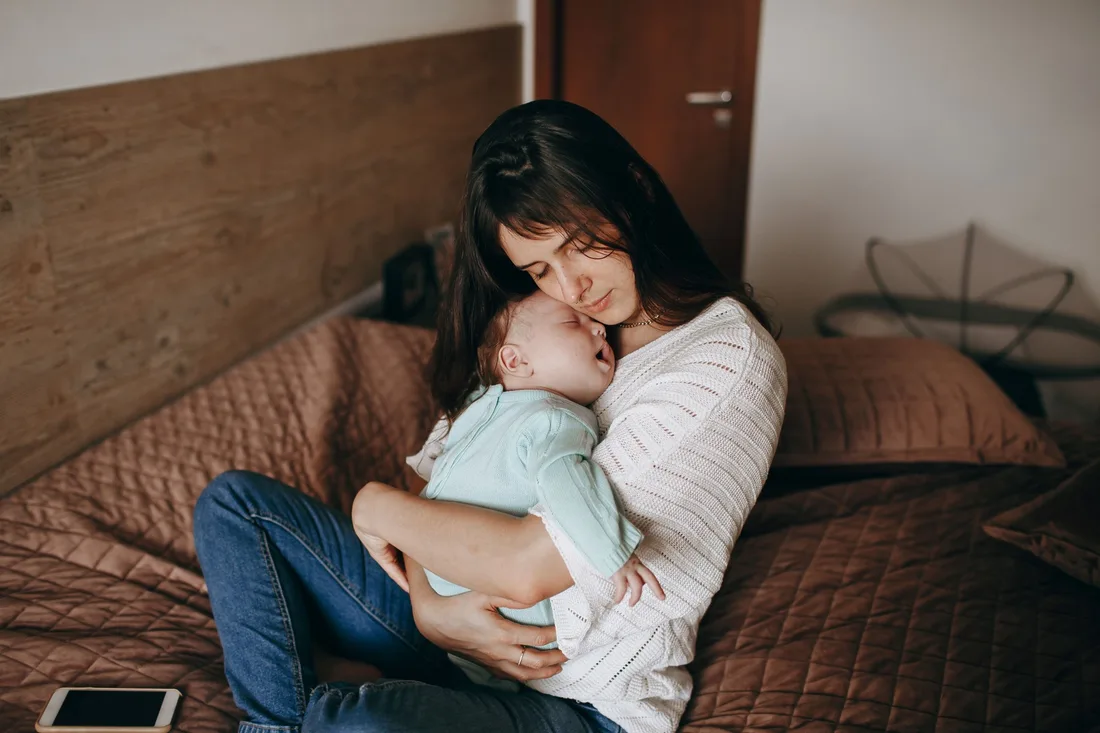 A mother sitting up and cradling her sleeping baby.